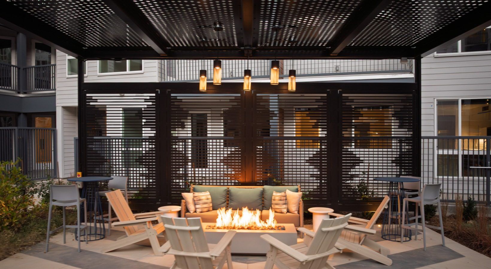 Chairs around a fire table under a steel pergola at dusk
